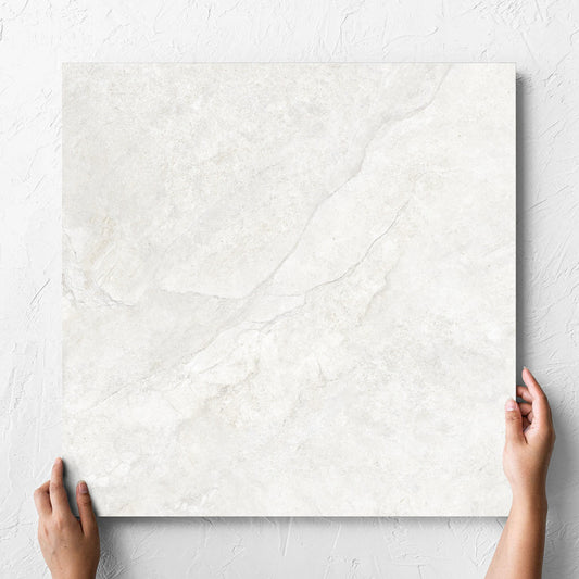 Hand holding a single Lakestone White Matt 600x600mm tile against a white rendered wall, showing the matt surface