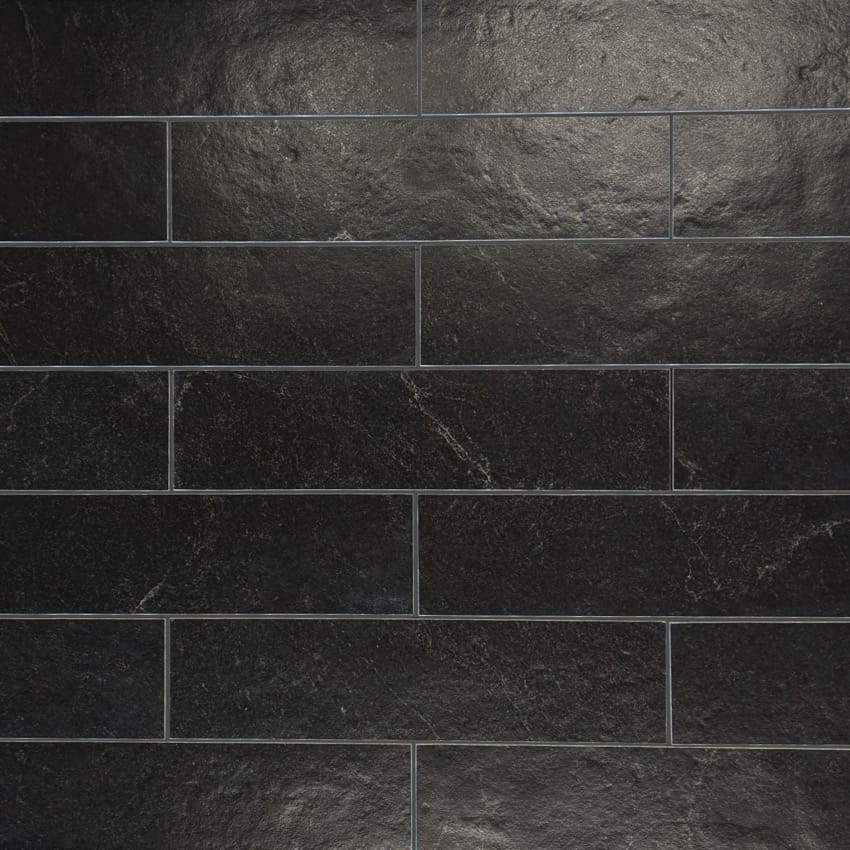 Close-up texture shot of Lava Black Amber Brick/Subway 75x300mm tiles showing a dark slate-effect surface with natural veining in a staggered brick layout.