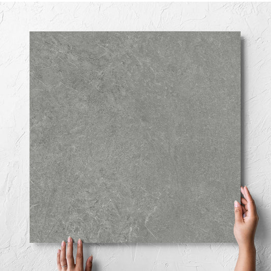 Hand holding a single Lava Grey Amber 600x600mm tile against a white rendered wall, showing the grey lappato surface