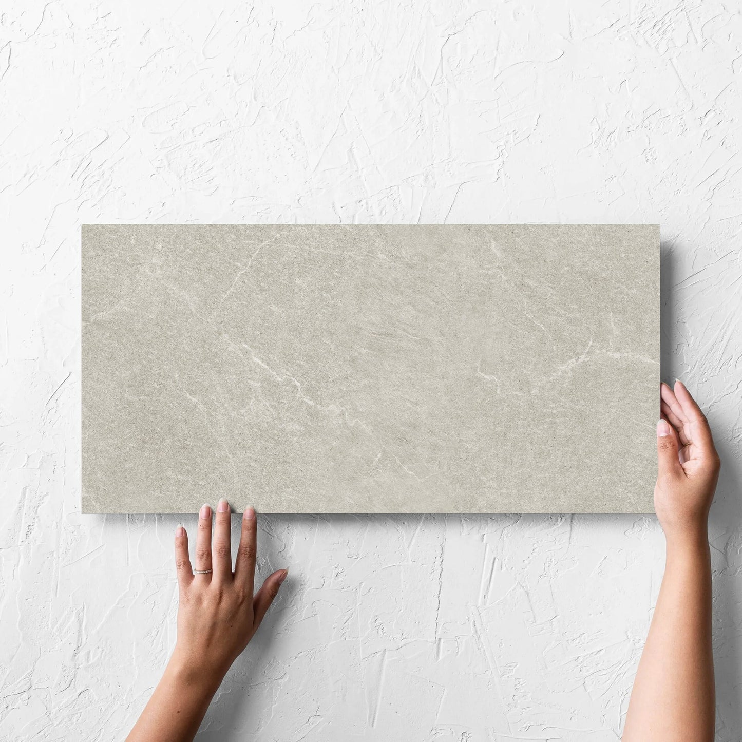 Hand holding a single Lava Soft Beige Amber 300x600mm tile against a white rendered wall, showing the soft beige lappato surface