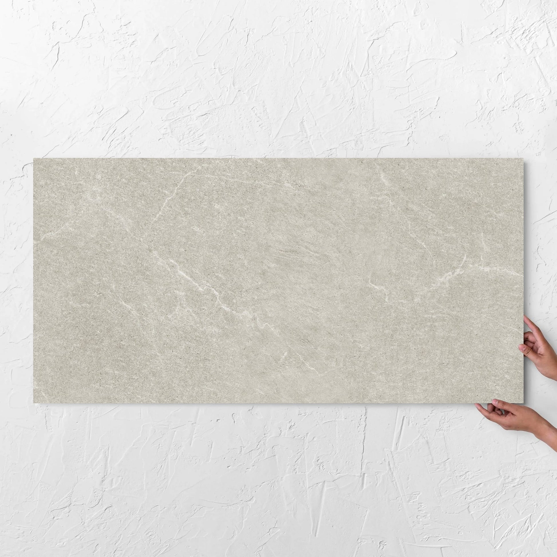 Hands holding a Lava Soft Beige Amber 600x1200mm tile against a white rendered wall, showing the tile surface