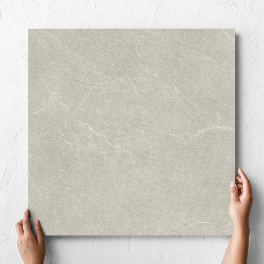 Hand holding a single Lava Soft Beige Amber 600x600mm tile against a white rendered wall, showing the soft beige lappato surface