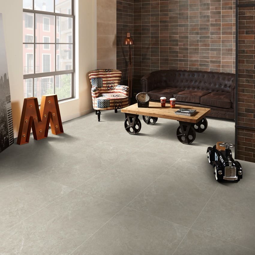 Lava Soft Beige Amber 600x600mm tiles laid as a large-format floor in an industrial-style living room featuring a leather sofa and wheeled coffee table.