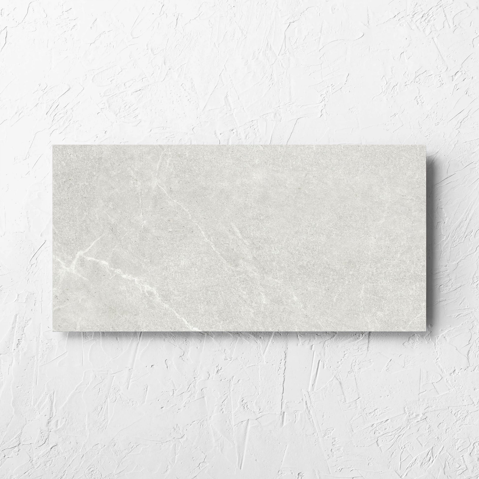 Lava Warm Grey Amber 300x600mm tile laid flat on a white rendered wall, showing the lappato surface