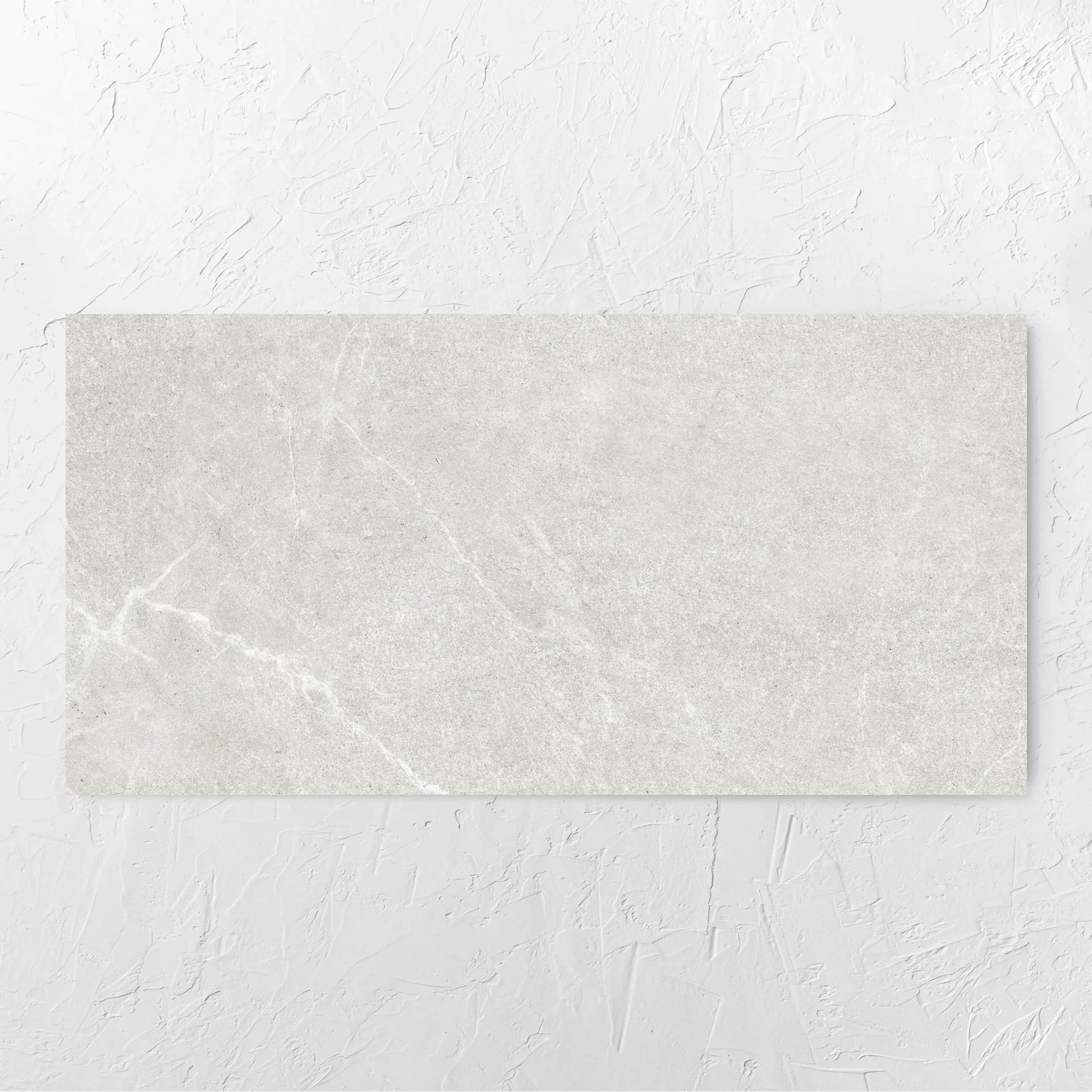 Lava Warm Grey Amber 600x1200mm tile laid flat on a white rendered wall, showing the warm grey surface