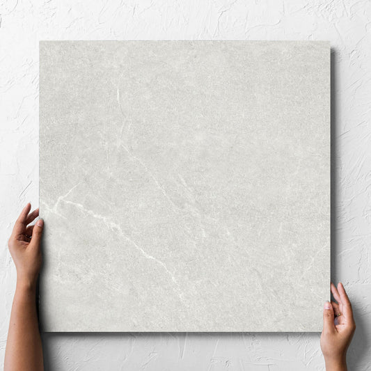 Hand holding a single Lava Warm Grey Inout 600x600mm tile against a white rendered wall, showing the tile surface