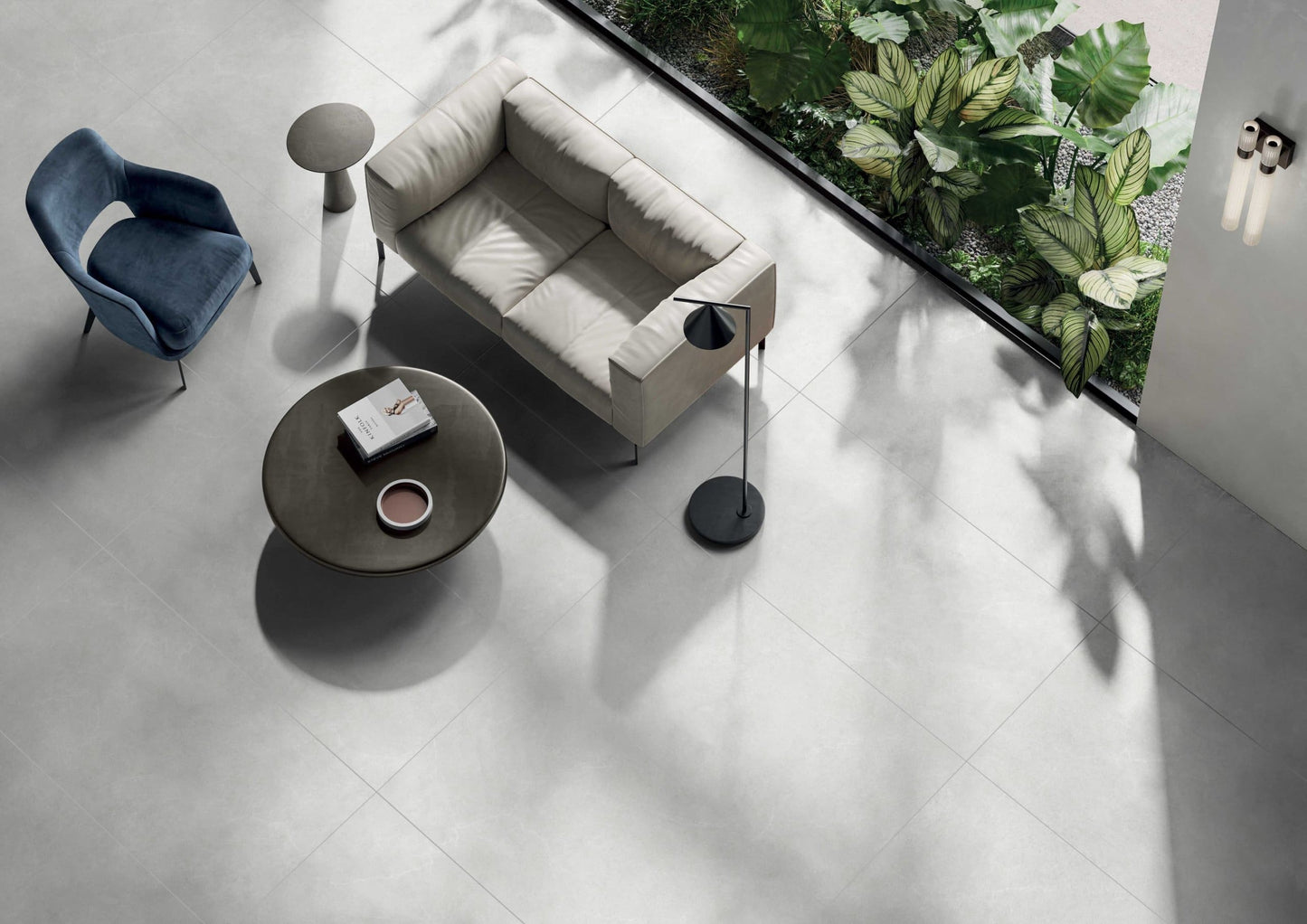 Lava White 600x600mm porcelain floor tiles installed in a modern living room with a light grey sofa, blue accent chair, and tropical garden view.