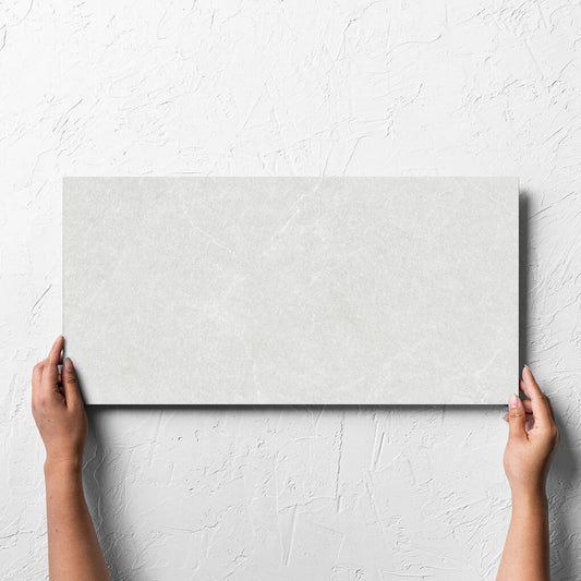 Hand holding a single Lava White Amber 300x600mm tile against a white rendered wall, showing the tile surface