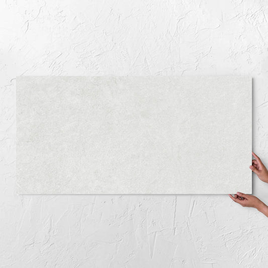 Hands holding a Lava White Amber 600x1200mm tile against a white rendered wall, showing the tile surface