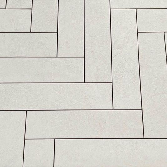 Close-up of Lava White Amber Brick/Subway 75x300mm tiles laid in a herringbone pattern with dark grout lines on a light stone-effect surface.