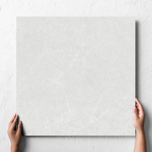 Hand holding a single Lava White Inout 600x600mm tile against a white rendered wall, showing the white lappato surface