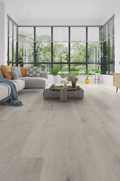 Light Grey Elegant SPC Hybrid 6.5mm Flooring 5+1.5mm installed in a bright open-plan living room with a grey sectional sofa and floor-to-ceiling windows.