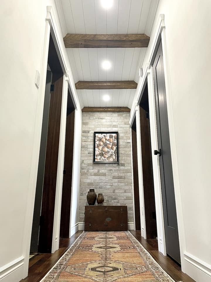 London Fog Brick Tile 60x250mm installed as a hallway feature wall with timber ceiling beams, dark wood trunk, and decorative ceramic vases.