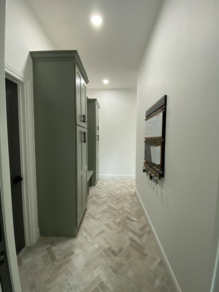 London Fog Brick Tile 60x250mm laid in a herringbone pattern on a mudroom hallway floor beside sage green cabinetry and a wall-mounted key organiser.