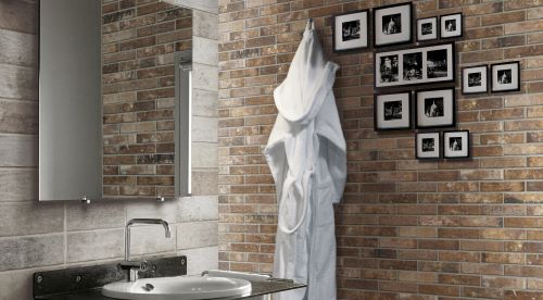 London Multicolor Brick Tile 60x250mm installed as a warm-toned bathroom feature wall alongside a wall-mounted vanity, mirror, and framed black-and-white photographs.