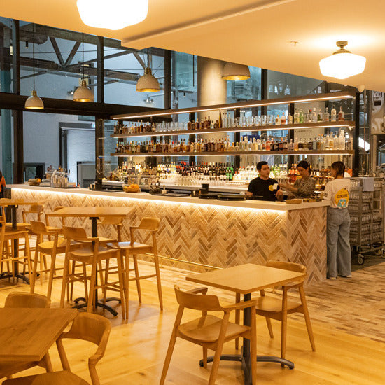 London Sunset Brick Tile 60x250mm installed in a herringbone pattern on a warm-toned bar counter front, complemented by wooden stools and pendant lighting.