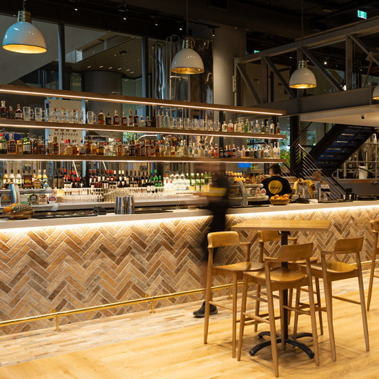 London Sunset Brick Tile 60x250mm installed in a herringbone pattern on a restaurant bar fascia, complemented by warm pendant lighting and timber bar stools.