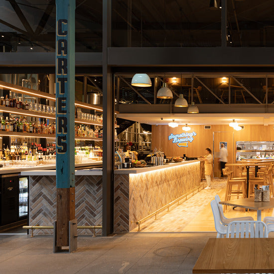 London Sunset Brick Tile 60x250mm installed in a herringbone pattern on a warm-toned restaurant bar front beneath pendant lights.