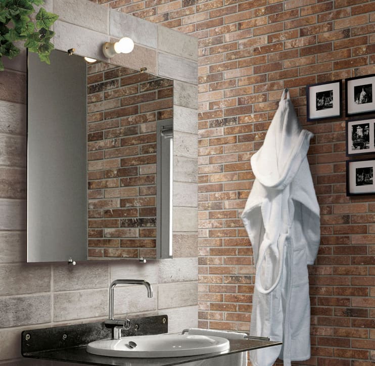 London Sunset Brick Tile 60x250mm installed in a rustic bathroom featuring warm terracotta tones, a white ceramic basin, wall mirror, and hanging bathrobe.
