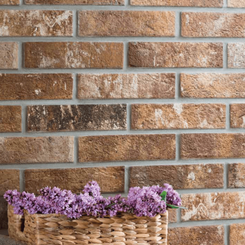 London Sunset Brick Tile 60x250mm installed as a rustic feature wall in warm amber and brown tones, styled with a wicker basket of purple lavender flowers.