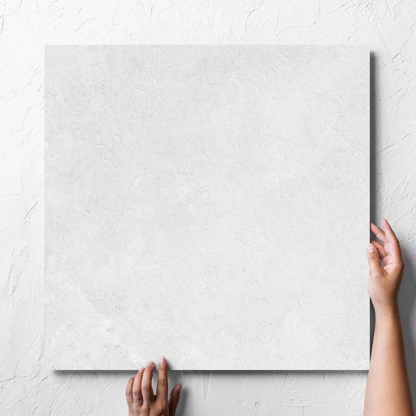 Hand holding a single Lusso Bianco Amber 600x600mm tile against a white rendered wall, showing the matt surface