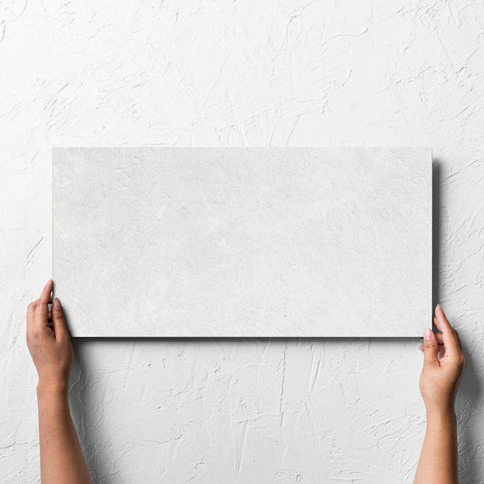 Hand holding a single Lusso Bianco Matt 300x600mm tile against a white rendered wall, showing the matt surface