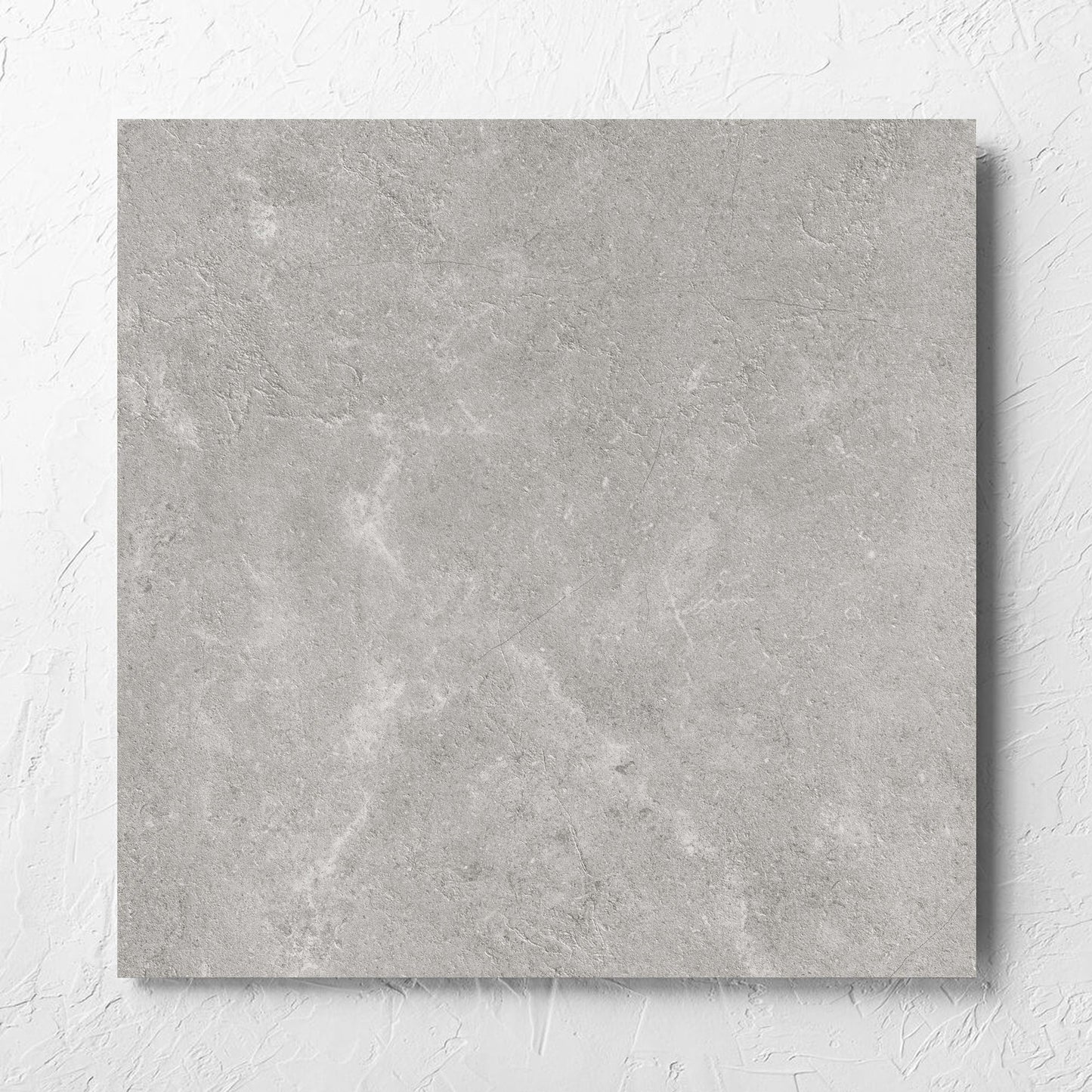 Lusso Grigio Amber 600x600mm tile laid flat on a white rendered wall, showing the matt surface