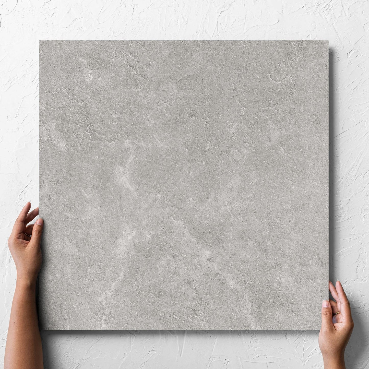 Hand holding a single Lusso Grigio Matt 600x600mm tile against a white rendered wall, showing the matt surface