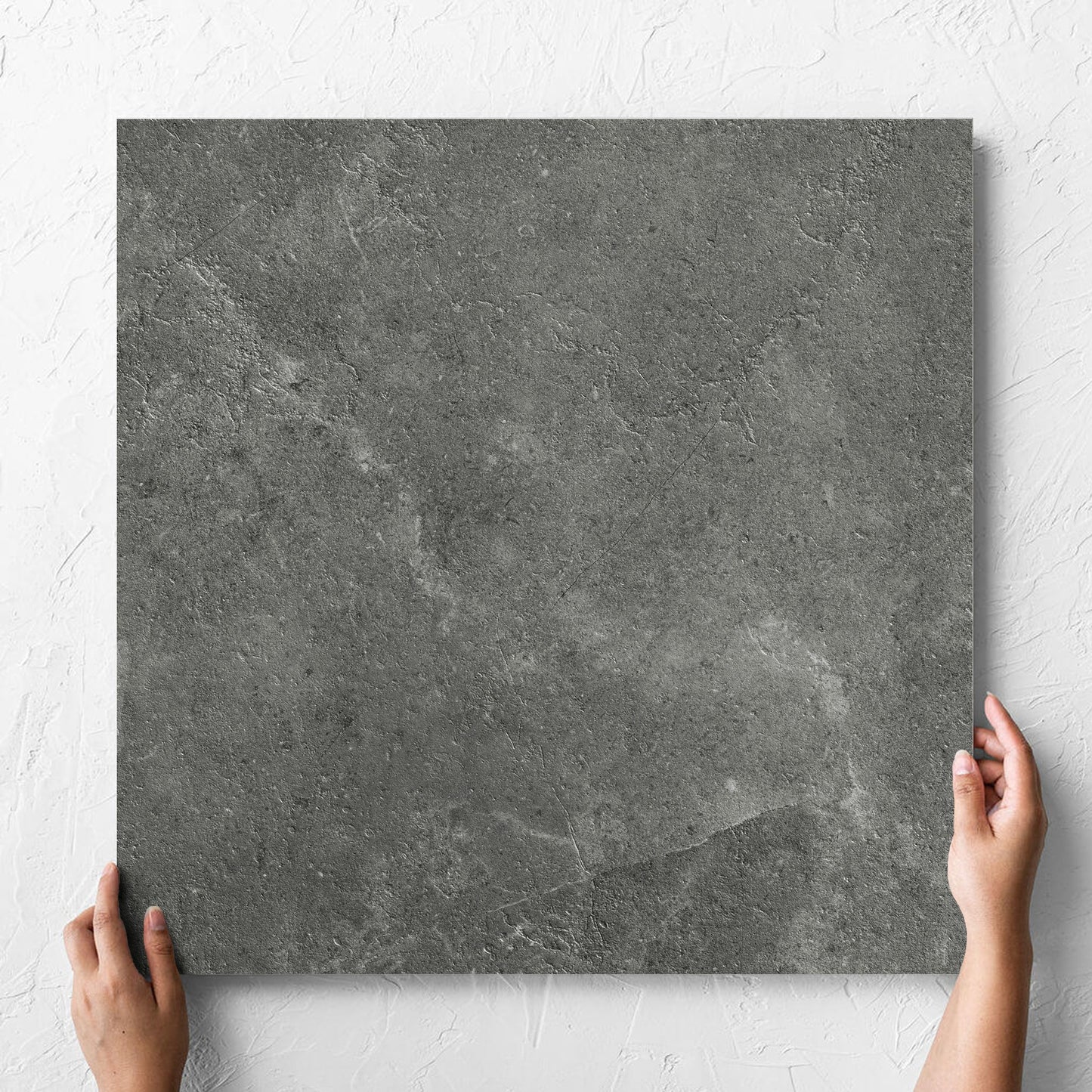 Hand holding a single Lusso Midnight Amber 600x600mm tile against a white rendered wall, showing the matt surface