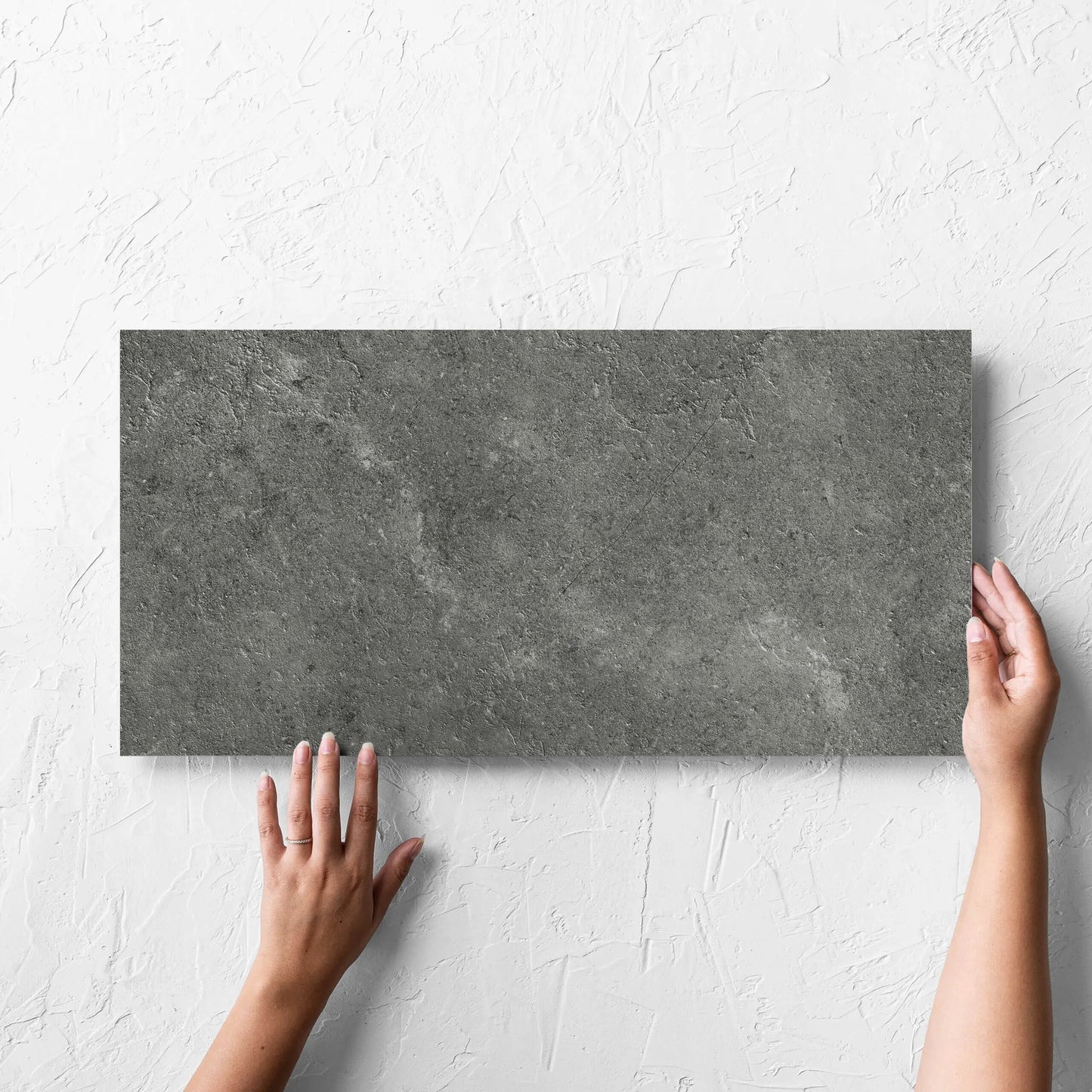 Hand holding a single Lusso Midnight Matt 300x600mm tile against a white rendered wall, showing the matt surface