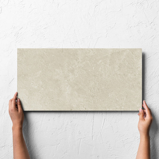 Hand holding a single Lusso Naturale Amber 300x600mm tile against a white rendered wall, showing the matt surface