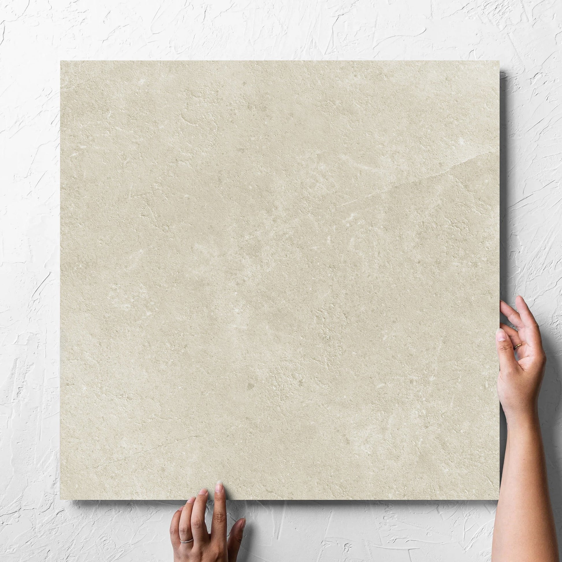 Hand holding a single Lusso Naturale Amber 600x600mm tile against a white rendered wall, showing the matt surface