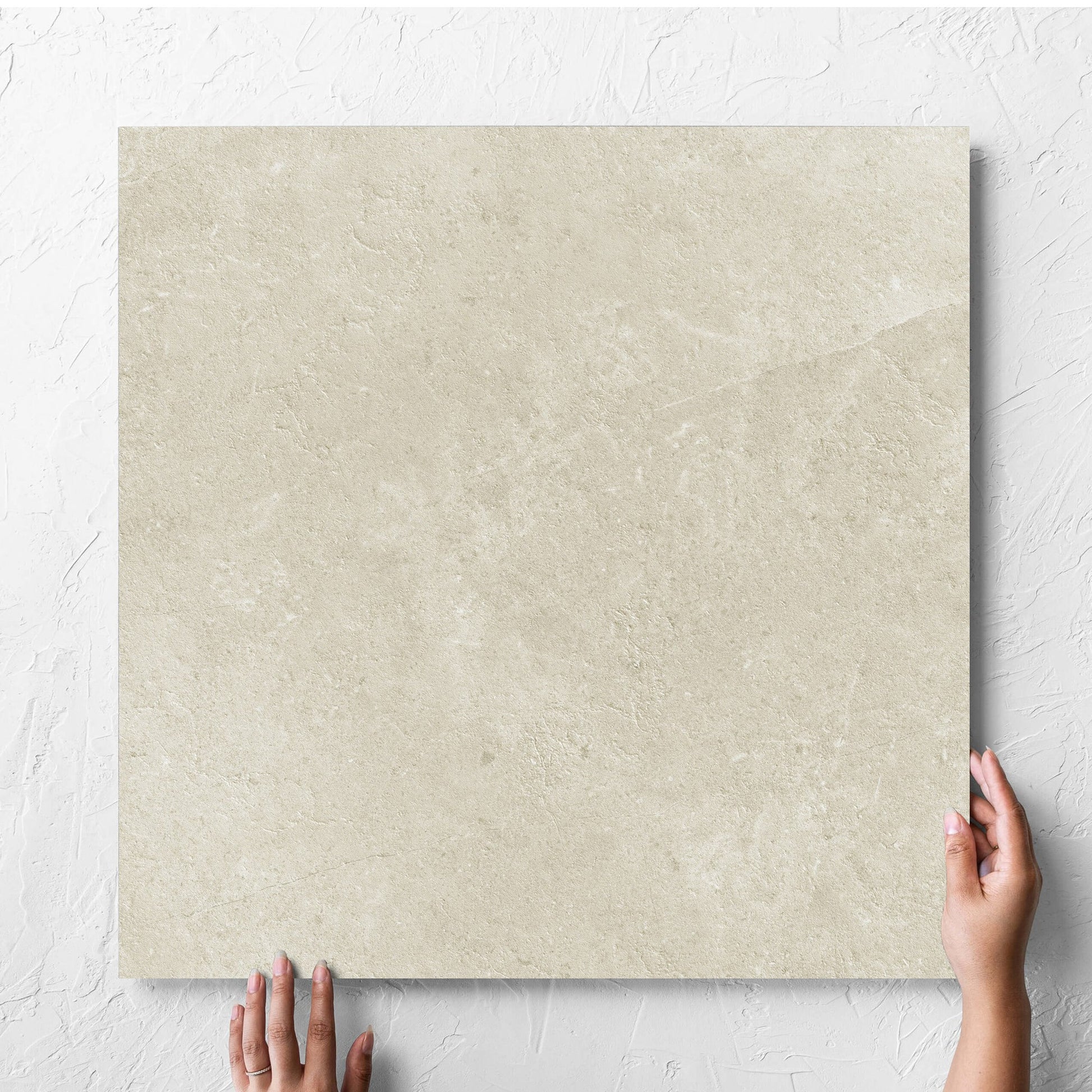 Hand holding a single Lusso Naturale Matt 600x600mm tile against a white rendered wall, showing the matt surface