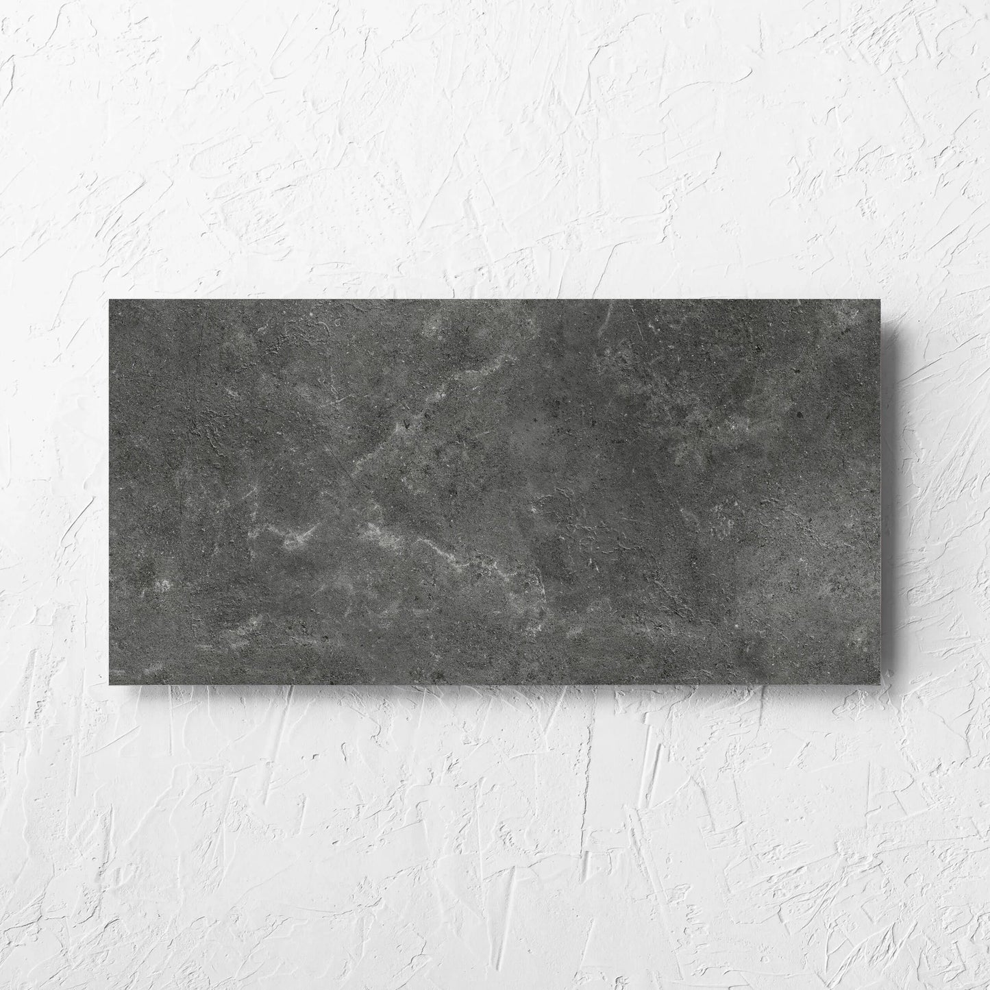 Lusso Nero Amber 300x600mm tile laid flat on a white rendered wall, showing the matt surface