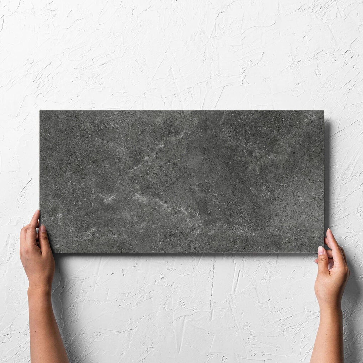 Hand holding a single Lusso Nero Matt 300x600mm tile against a white rendered wall, showing the matt surface