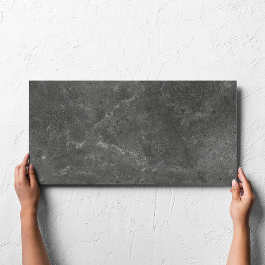 Hand holding a single Lusso Nero Matt 300x600mm tile against a white rendered wall, showing the matt surface