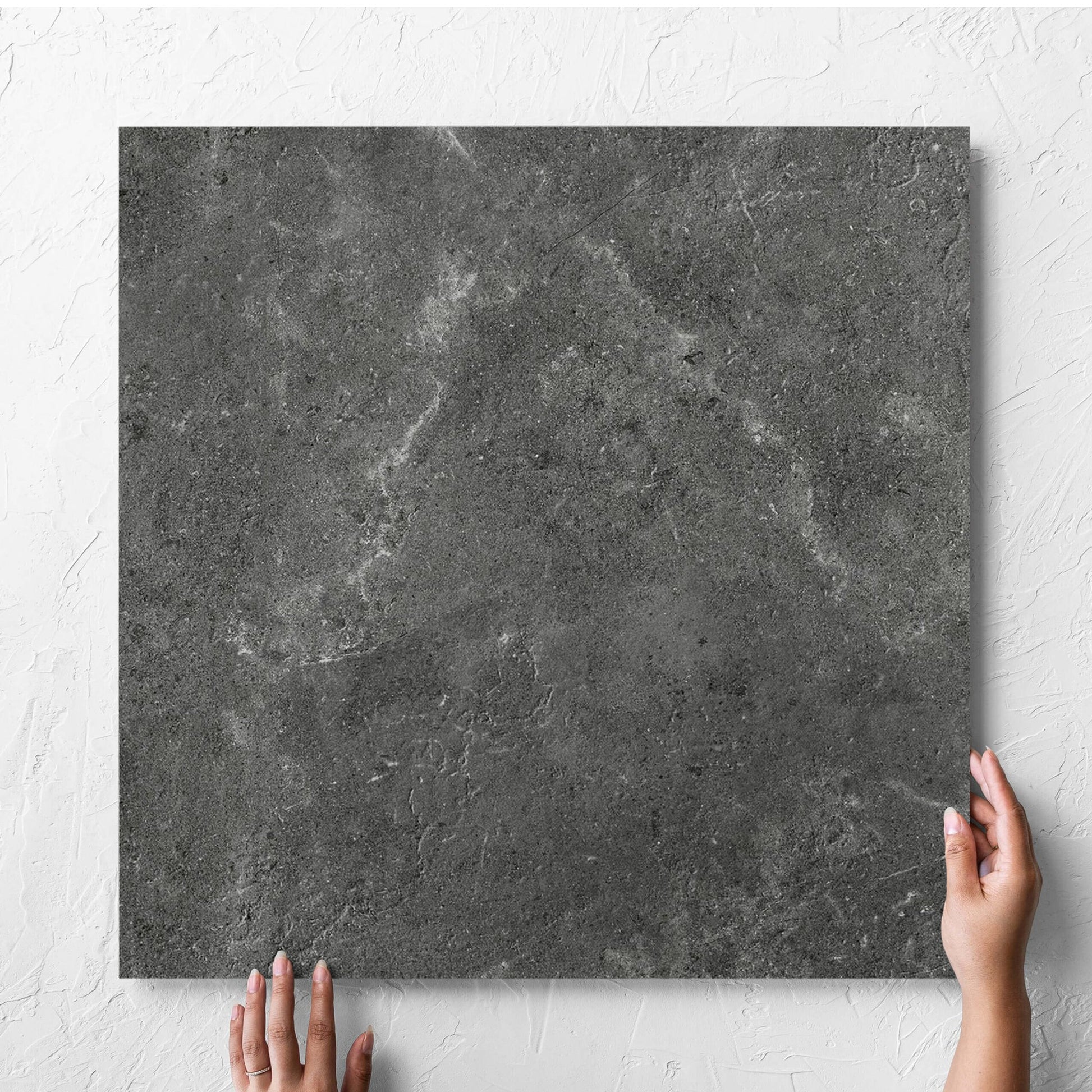 Hand holding a single Lusso Nero Matt 600x600mm tile against a white rendered wall, showing the matt surface