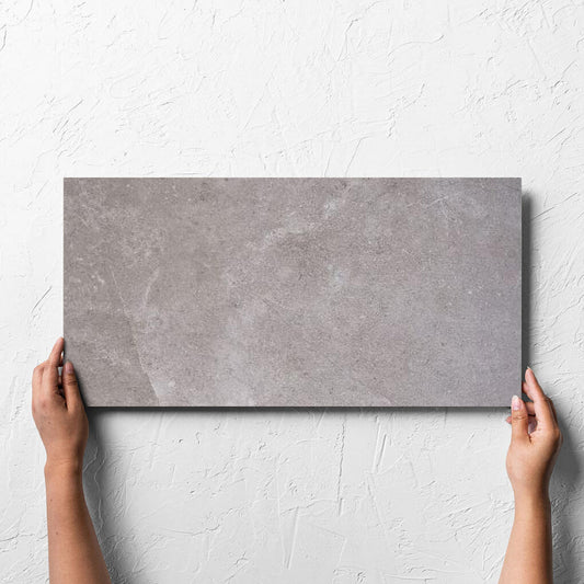 Hand holding a single Lusso Terra Amber 300x600mm tile against a white rendered wall, showing the matt surface