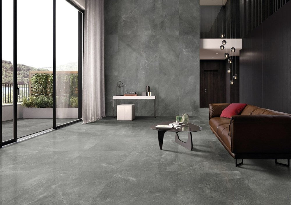Lusso Terra Amber 300x600mm large-format grey stone-effect tiles covering the floor and feature wall of a contemporary living room with leather sofa and pendant lights.