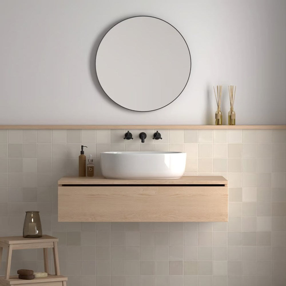 Majorca Gloss Off White 100x100mm tiles covering a bathroom wall behind a floating oak vanity with a round vessel sink and circular mirror.