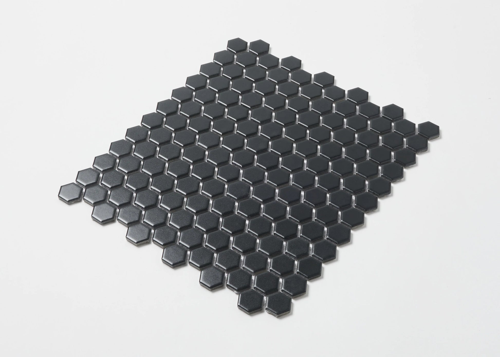 Pack shot of Marlowe Black Matt Mosaic Hexagon 23x23mm tiles arranged in a flat-lay sheet showing matte black hexagonal ceramic pieces with dark grout joints.