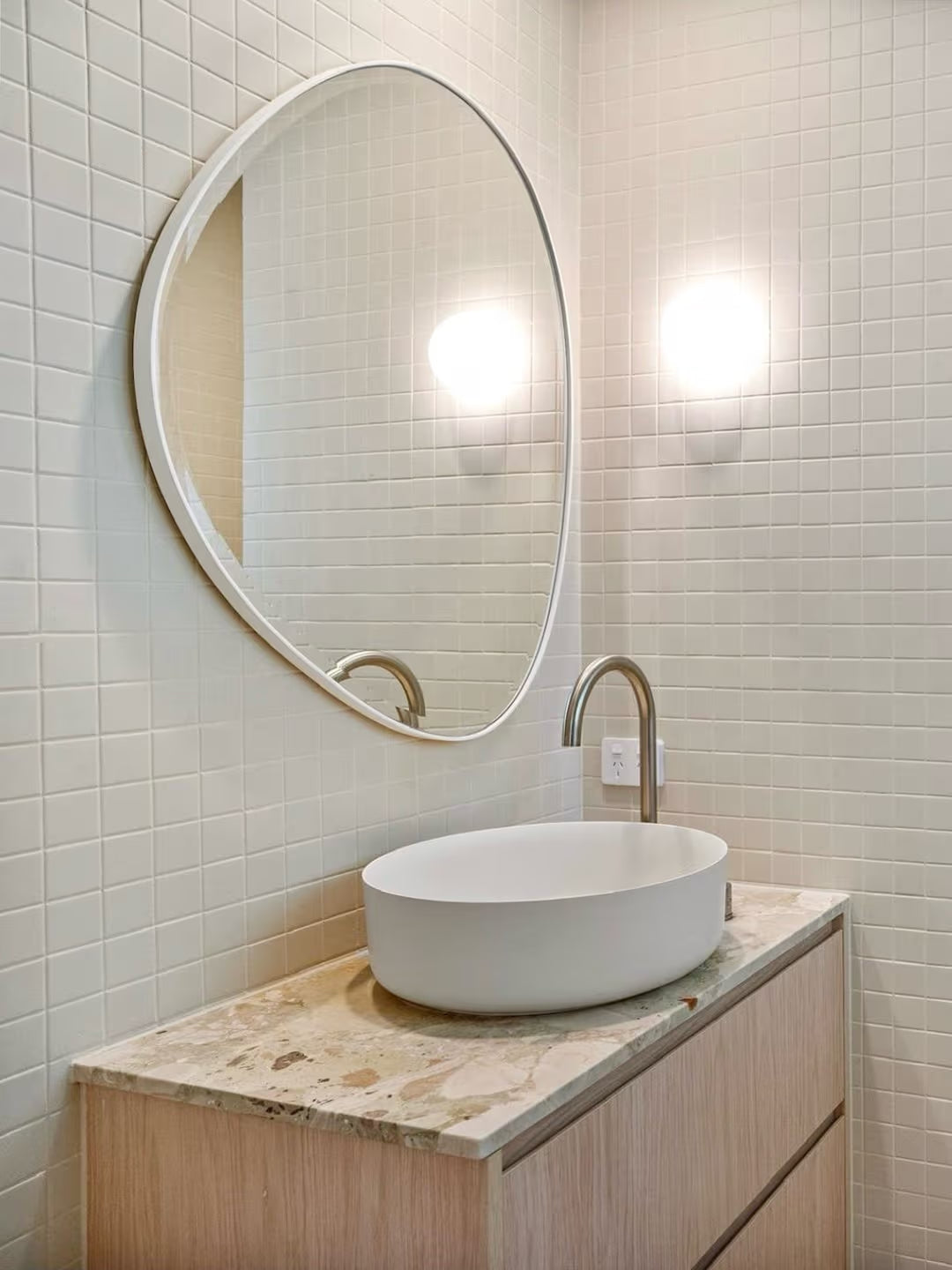 Marlowe Bone Matt Mosaic 48x48mm tiles cover a bright bathroom wall behind a round mirror, oval vessel sink, and brushed nickel tapware on a marble vanity top.