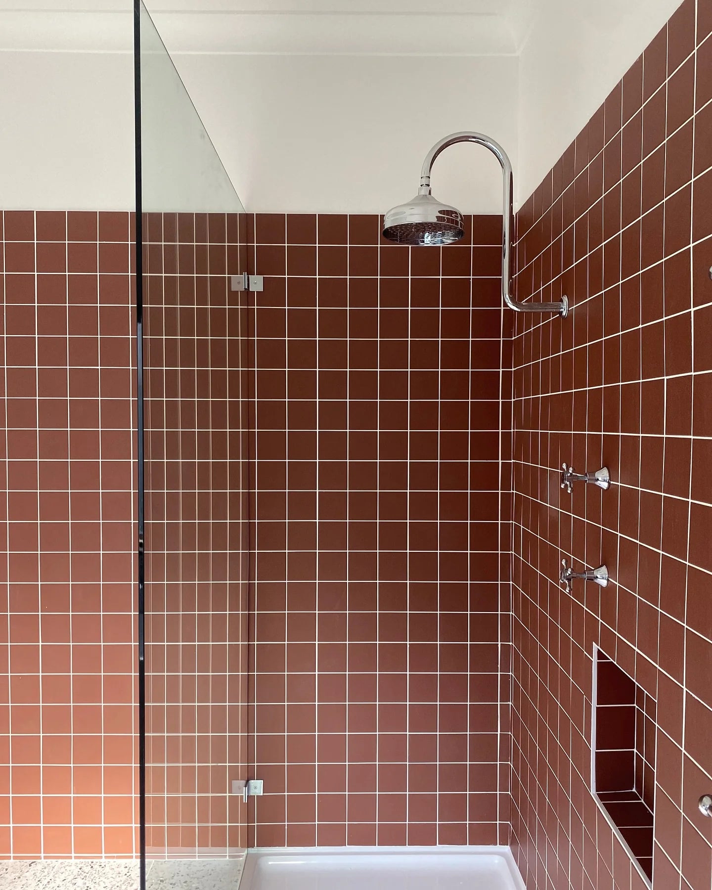 Marlowe Chestnut Red Matt Mosaic 97x97mm tiles covering a walk-in shower enclosure with chrome rainfall showerhead, twin wall-mounted tap fixtures, and recessed niche shelf.