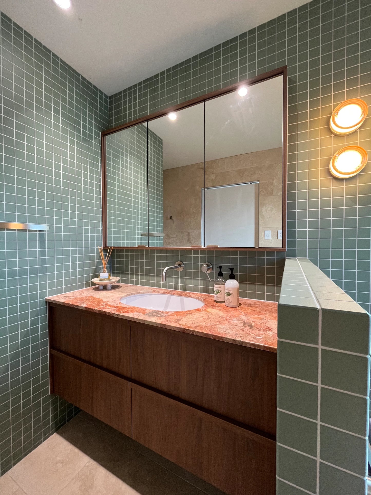 Marlowe Pistachio Green Matt Mosiac 48x48mm tiles covering bathroom walls alongside a floating timber vanity with pink marble countertop and warm globe wall sconces.