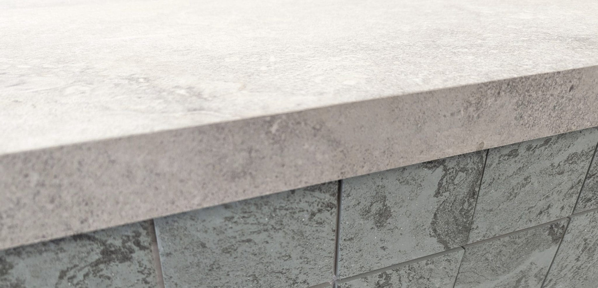 Mars Light External Pencil Bullnose 390.80x600x20mm shown as a light grey stone coping cap atop a dark grey textured tile wall, highlighting the bullnose edge profile.