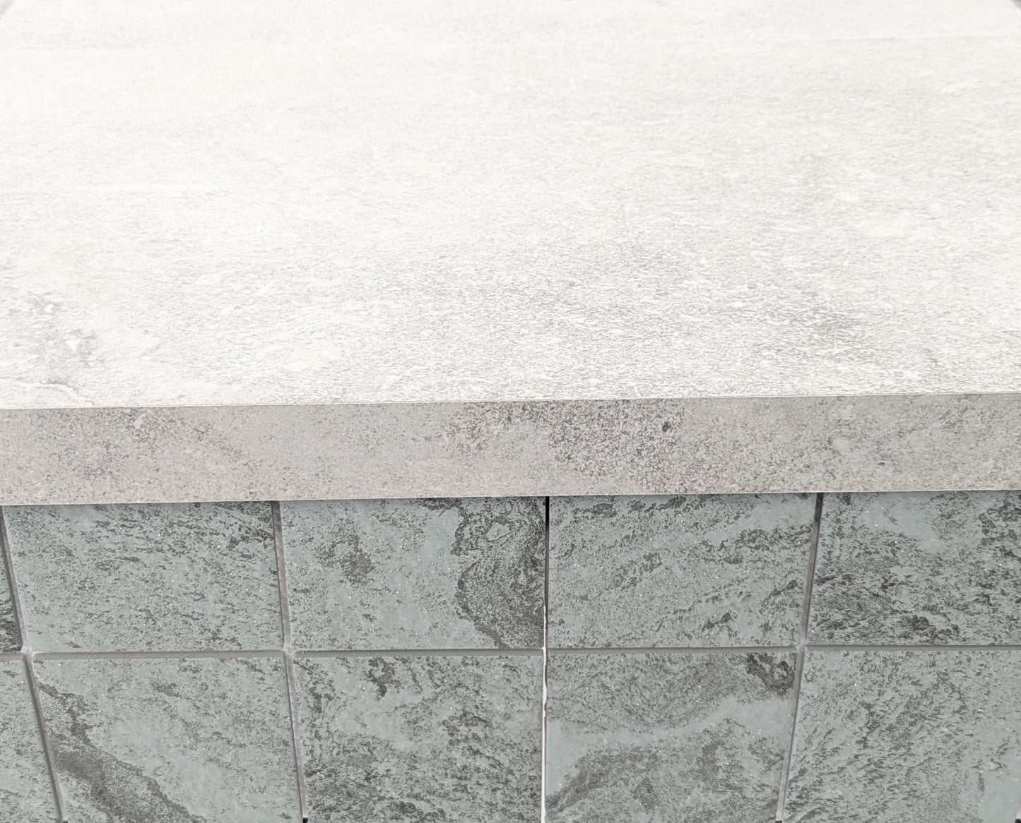 Mars Light External Pencil Bullnose 390.80x600x20mm installed as pool coping edge over dark grey textured stone wall tiles in an outdoor setting.