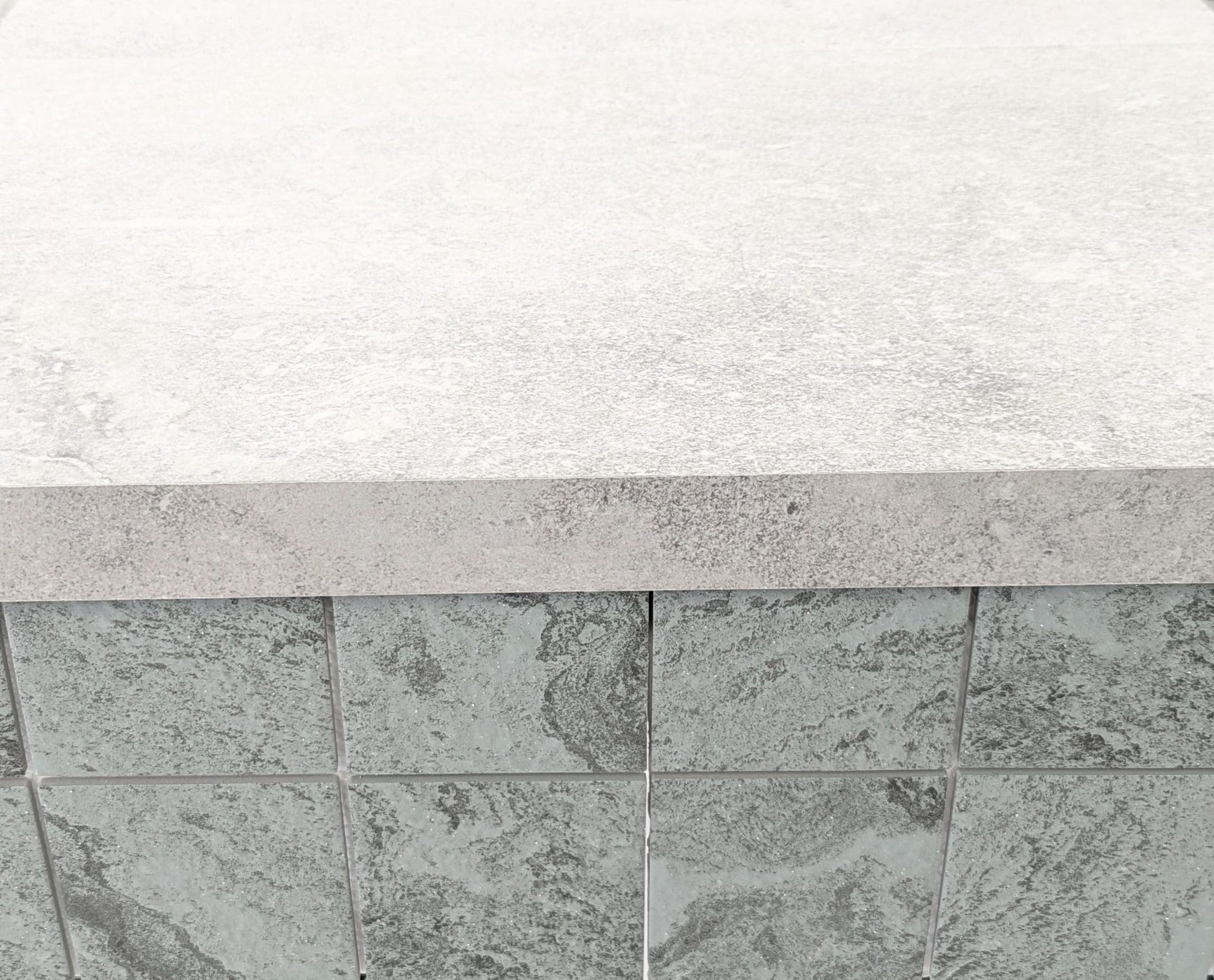Mars Light External Pencil Bullnose 390.80x600x20mm installed as pool coping edge over dark grey textured stone wall tiles in an outdoor setting.