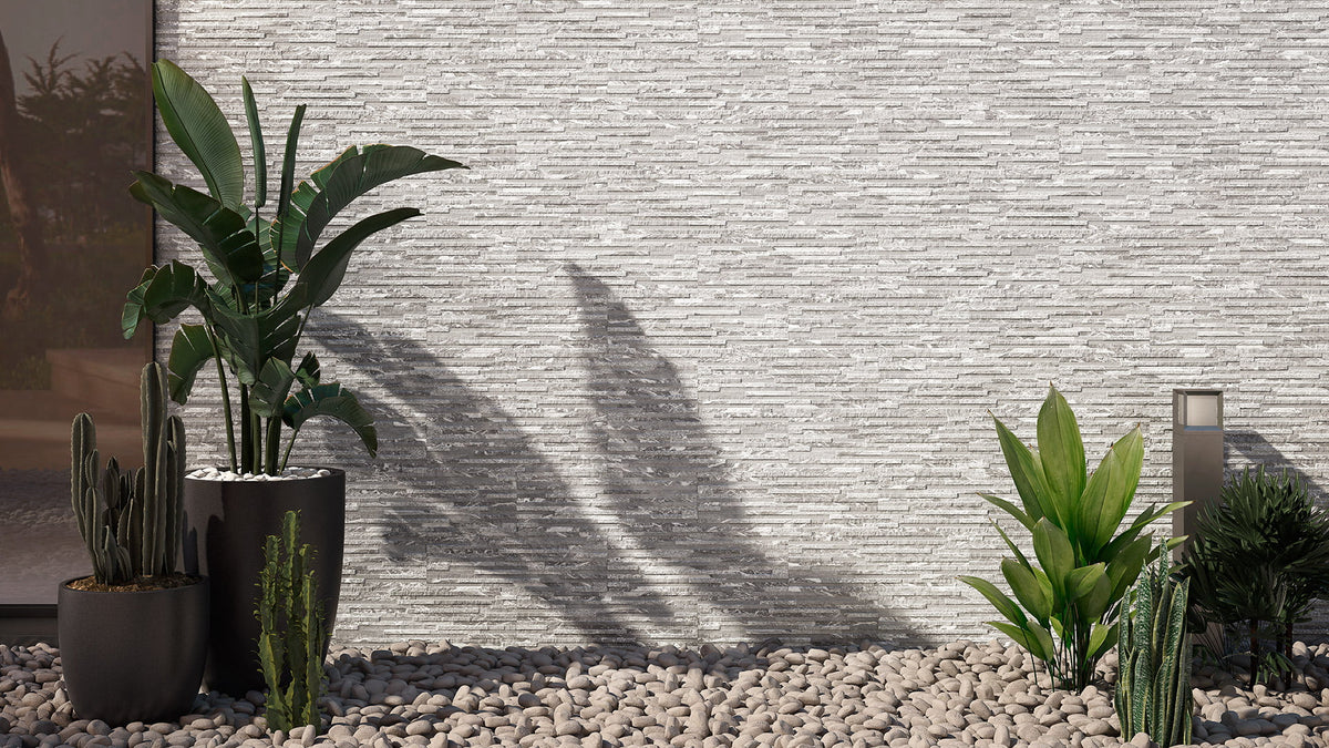 Maule Blanco Matt 170x520mm grey stacked-stone effect wall tiles installed on an outdoor facade surrounded by tropical potted plants and pebble garden bed.