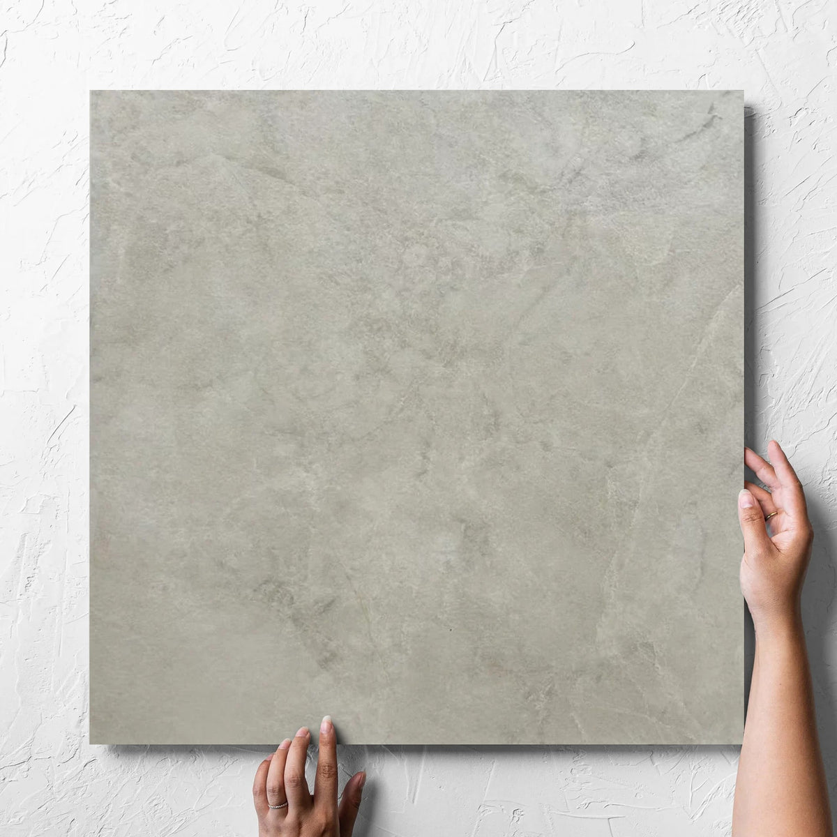 Hand holding a single Memory Stone Beige Matt 600x600mm tile against a white rendered wall, showing the tile surface