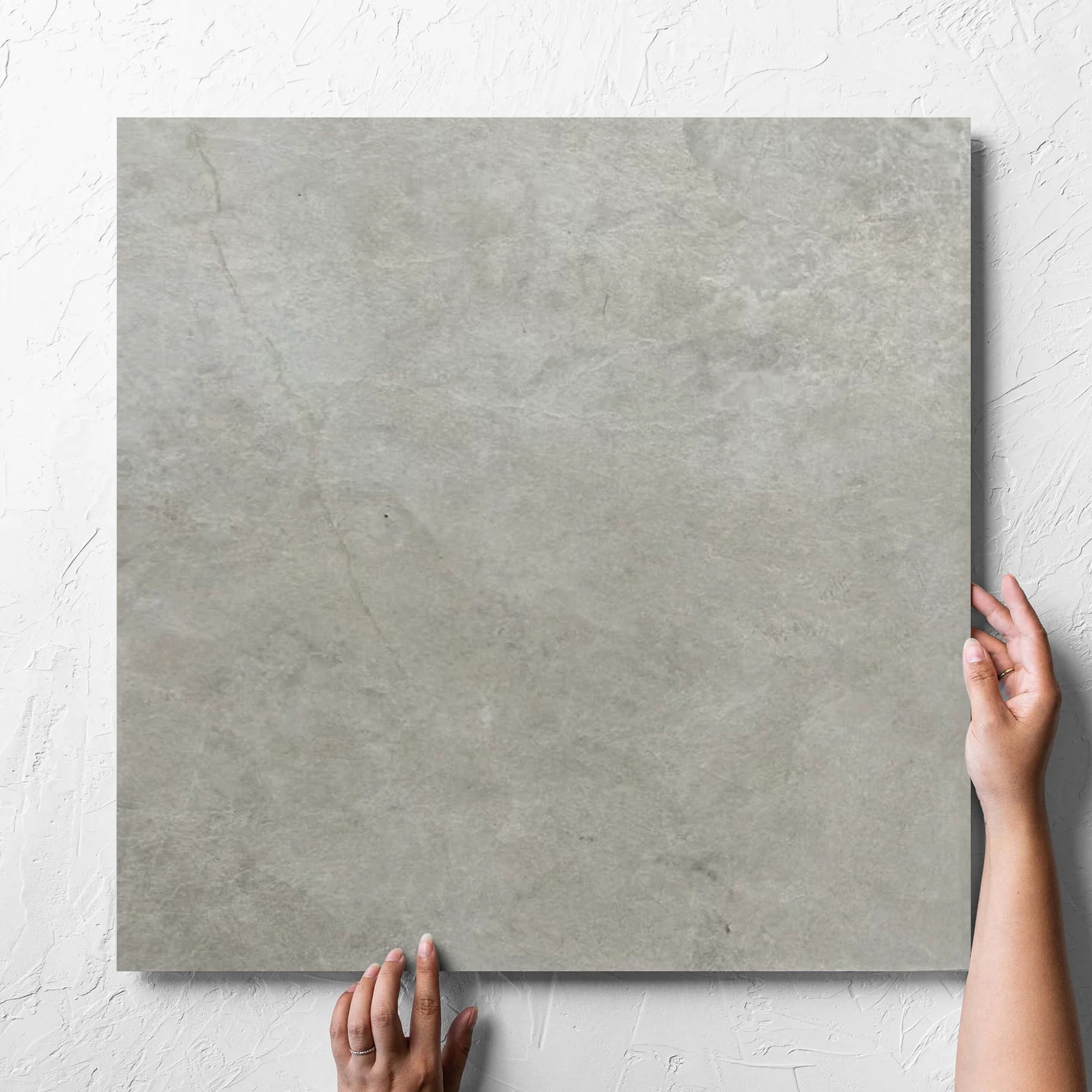 Hand holding a single Memory Stone Bianco Matt 600x600mm tile against a white rendered wall, showing the tile surface
